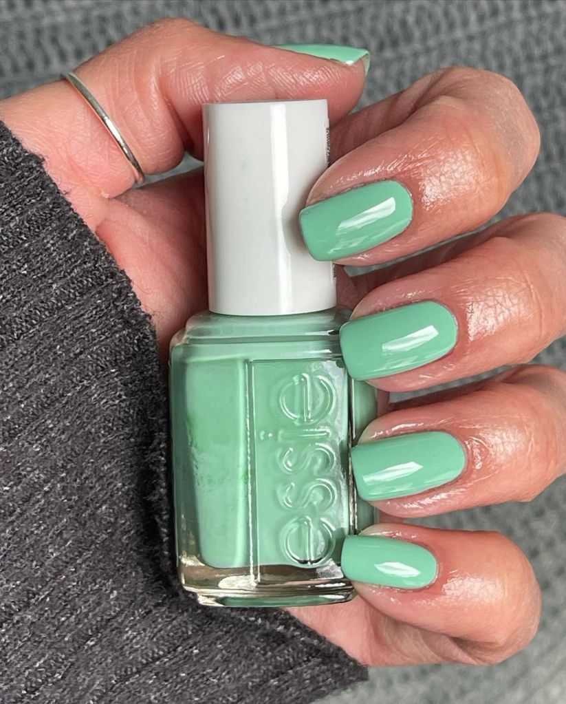 A woman's hand and finger nails wearing Essie green nail polish, It's High Time, summer 2023 nail trends