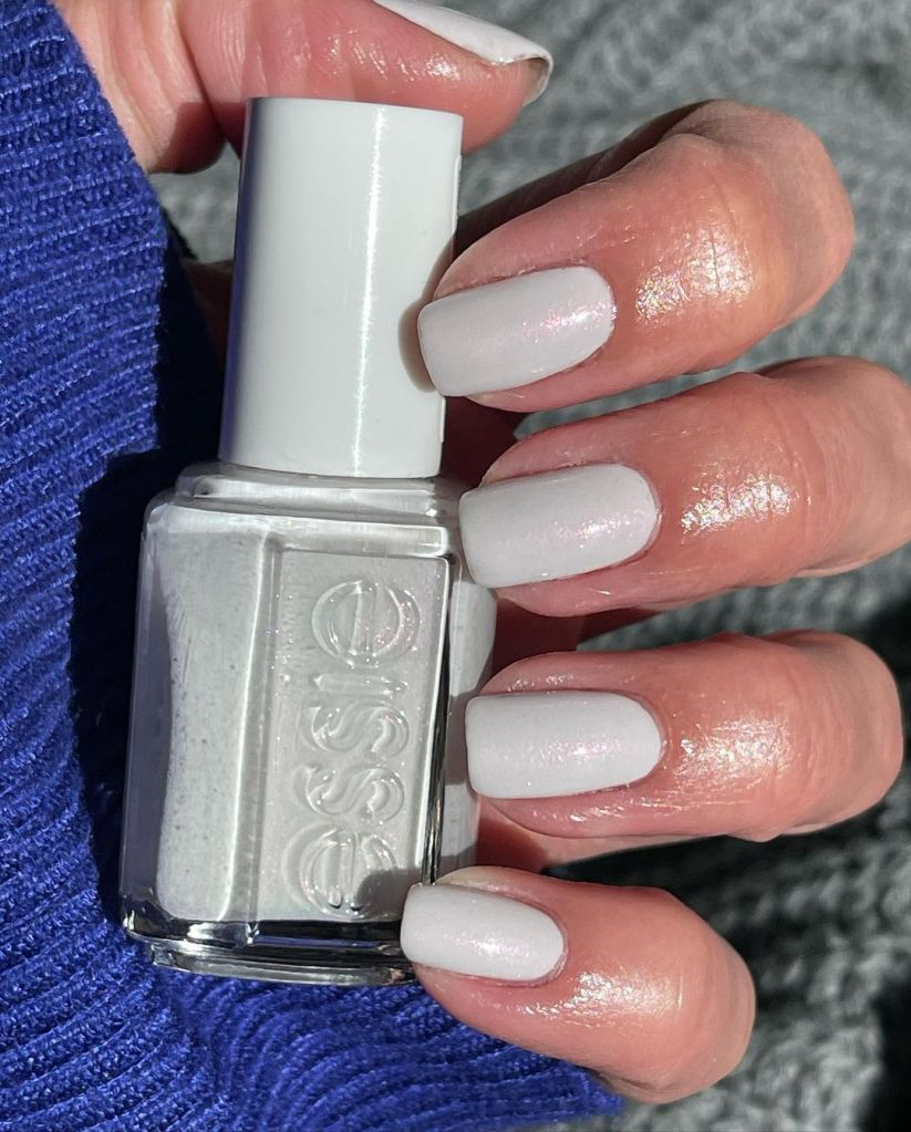 A woman's hand and finger nails wearing essie white iridescent in on the download, summer 2023 nail trends