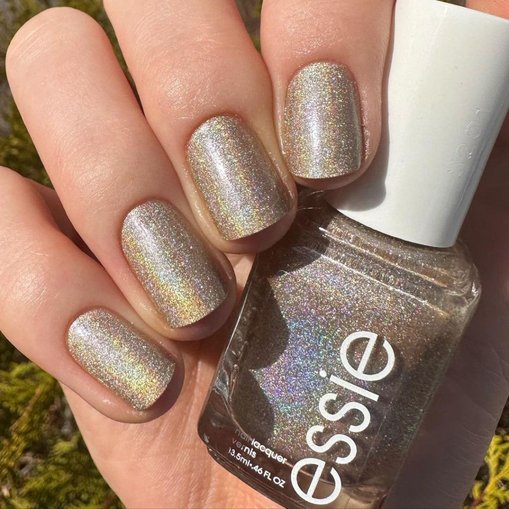 A woman's hand and finger nails wearing essie sparkly gold, metallic nail polish in semiprecious tones