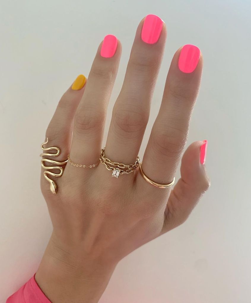 A woman's hand and finger nails wearing neon pink nail polish by Lisa Kon, summer 2023 nail trends