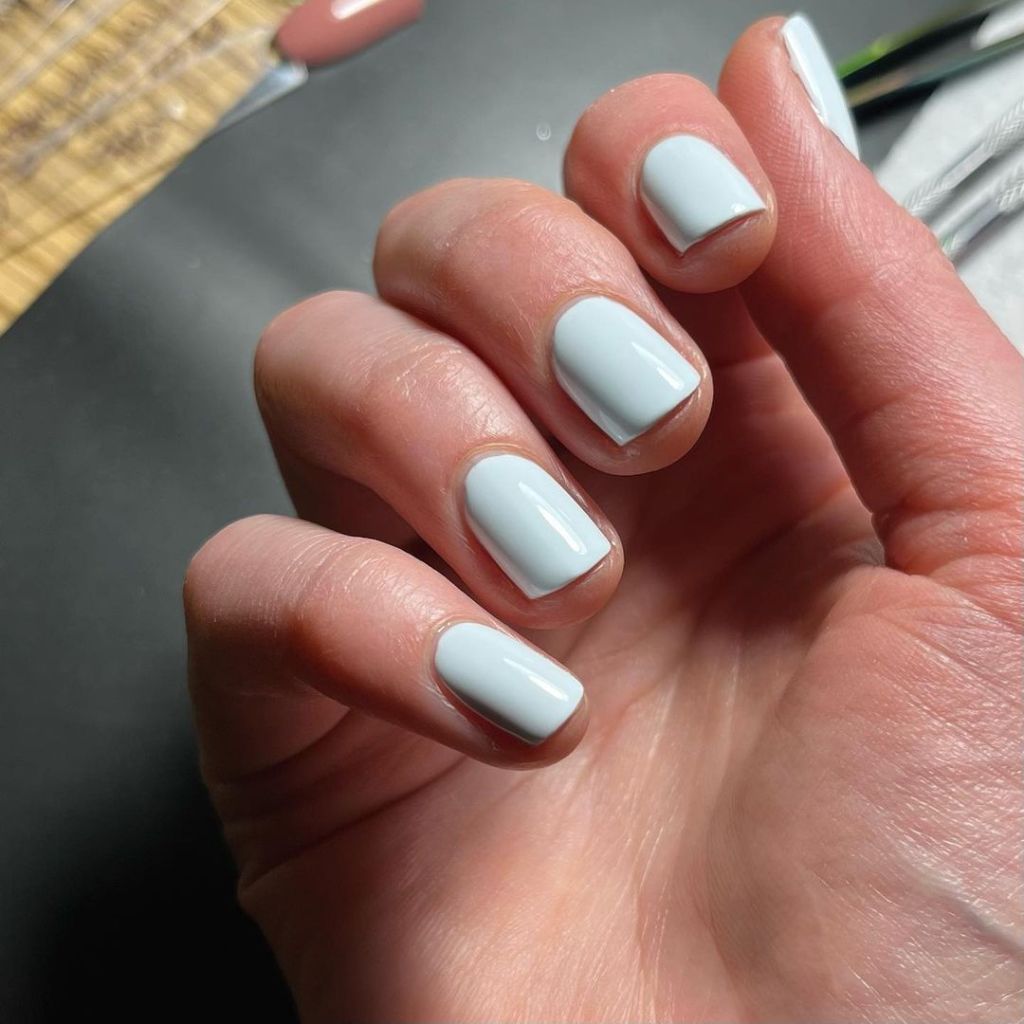 A woman's hand and finger nails wearing Olive Ave light blue nail polish, Cloudy, summer 2023 nail trends