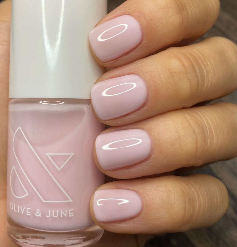 A woman's hand and finger nails wearing Olive & June light pink nail polish in strawberry scone